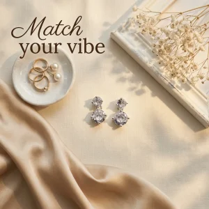 چیدمان زیبای گوشواره میخی دو نگین نقرهای آی ام روی پارچه کرم همراه با عبارت Match your vibe، قاب سفید و ظرف انگشتر